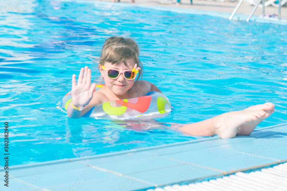 A child in a sunglasses is resting in the turquoise water of the pool. A little girl swims in the pool on an inflatable circle The concept of a fun children's holiday.