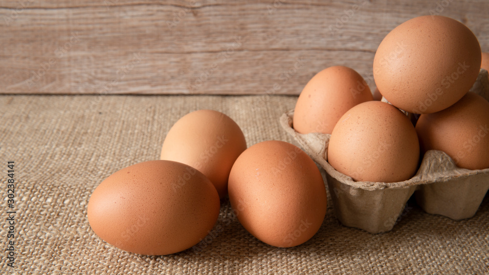 Brown chicken eggs in paper egg box on sackcloth and wooden background. Healthy food concept Brown chicken eggs in paper egg box on sackcloth and wooden background. Healthy food concept