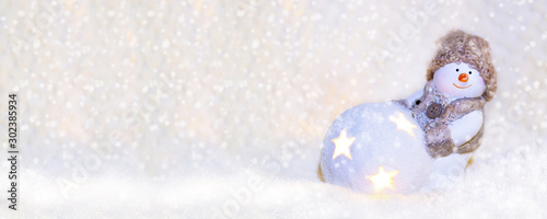 Picture for web banner. Toy snowman in a knitted hat, with a luminous ball close up on a white background. New Year and Christmas background for greetings, banner, postcard, advertisement, Copy space,