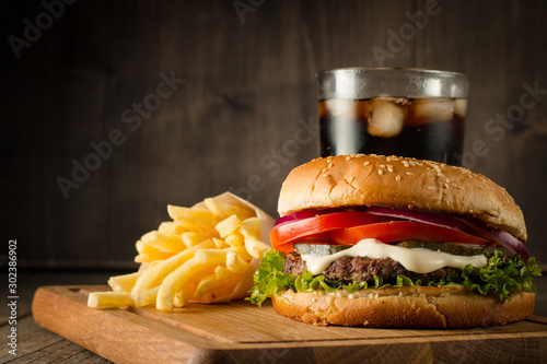 Home made hamburger with beef  onion  tomato  lettuce and cheese. Fresh burger close up on wooden rustic table with potato fries  beer and chips. Cheeseburger.
