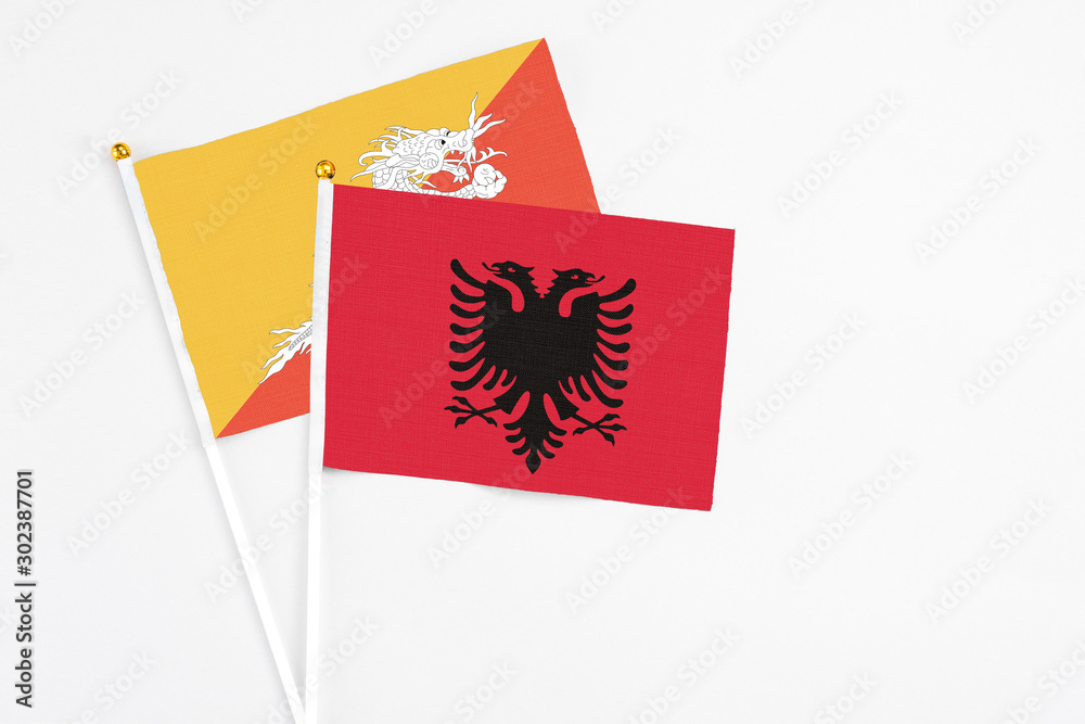Fototapeta premium Albania and Bhutan stick flags on white background. High quality fabric, miniature national flag. Peaceful global concept.White floor for copy space.
