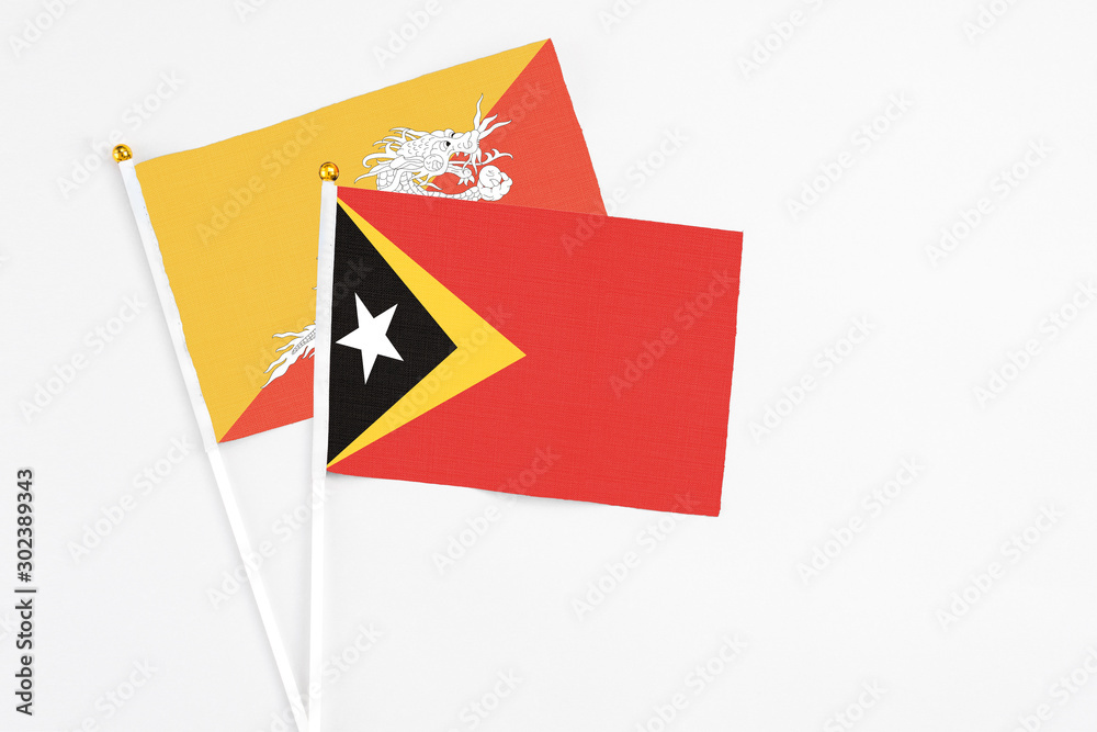 Obraz premium East Timor and Bhutan stick flags on white background. High quality fabric, miniature national flag. Peaceful global concept.White floor for copy space.