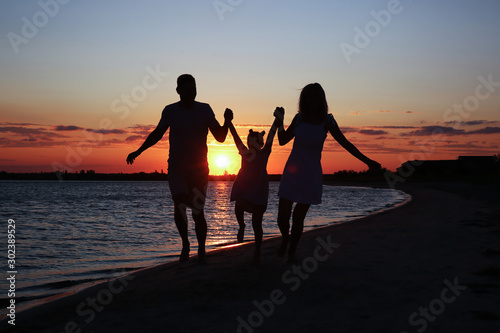 Silhouette of happy family on sea beach at sunset