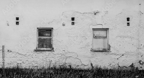 Old abandoned building broken facade white wall with windows, plaster falling off photo