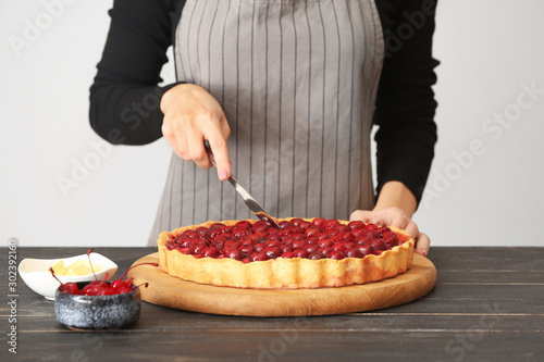 Woman cutting tasty cherry pie at table