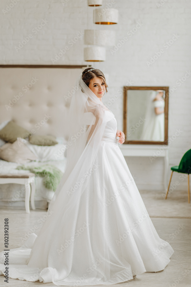 Pretty bride in a white dress stands in a room by the bed Pretty bride in a white dress stands in a room by the bed