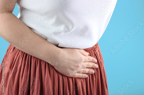 Girl in a white t-shirt and skirt holding her belly, concept of menstruation pain © TATIANA