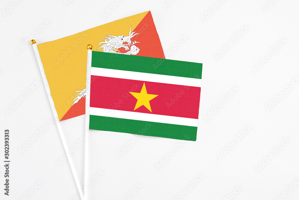 Suriname and Bhutan stick flags on white background. High quality fabric, miniature national flag. Peaceful global concept.White floor for copy space.