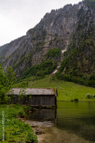 Holzhütte an einem Bergsee mit Wald und Bergen an einem regnerischen woligen Sommertag