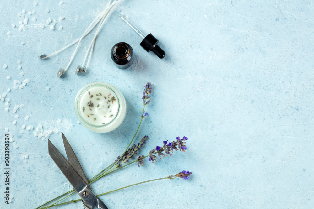 Handmade lavender scented candle with essential oil, flowers, wax, wicks, and scissors, flatlay, shot from above with copy space. An artisanal Christmas gift, zero waste Christmas concept, toned image - obrazy, fototapety, plakaty 