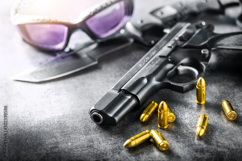 Detail of 9mm pistol, bullets and handcuffs. Gun with ammunition on dark stone background.