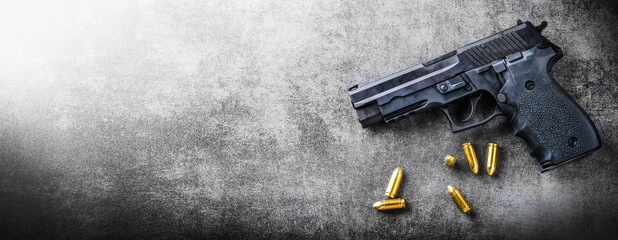 Hand gun banner or panorama pfoto on dark stone table top view. Ammunition or bullets at black background. Copy space for text concept.