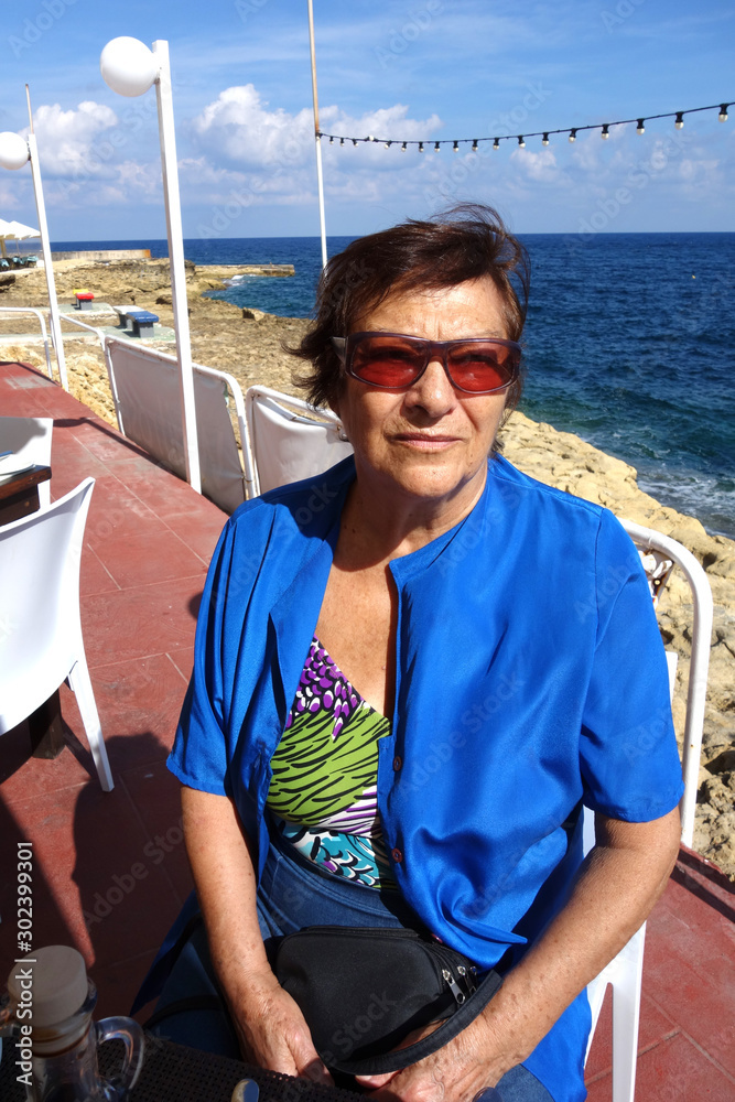 Retired elderly woman wearing sunglasses sitting at the restaurant at the seaside