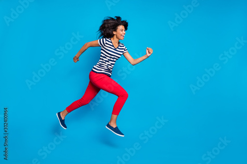 Fototapeta Naklejka Na Ścianę i Meble -  Side profile full length body size photo of cheerful laughing cute nice pretty girlfriend jumping running towards shopping center isolated vivid blue color background