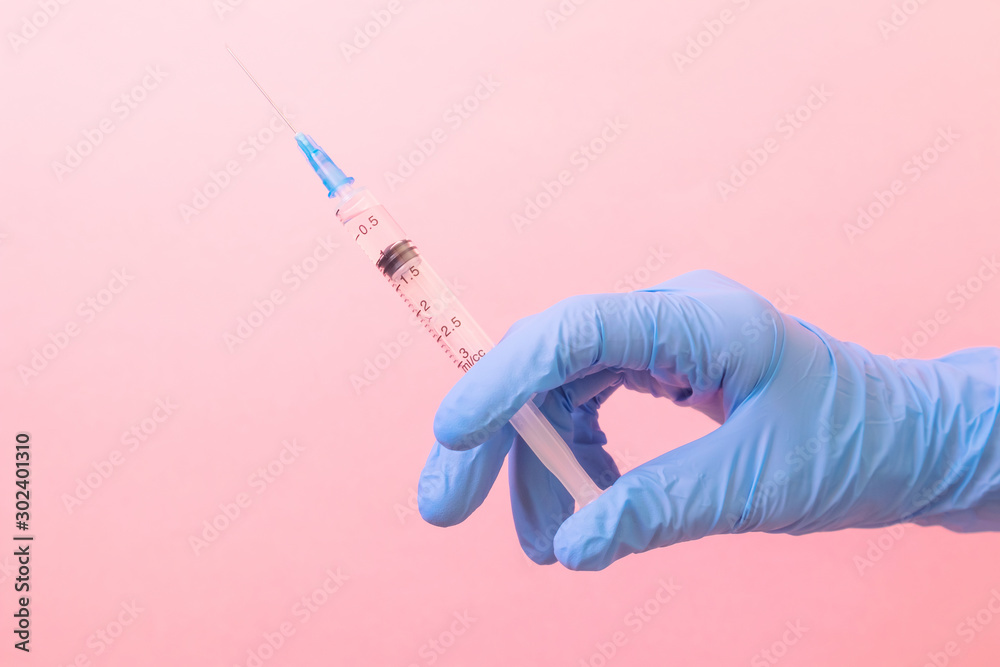 Hand in a blue medical glove with a syringe on a pink background. The concept of medicine, vaccination, health. Minimalism, place for text. Hand in a blue medical glove with a syringe on a pink background. The concept of medicine, vaccination, health. Minimalism, place for text.