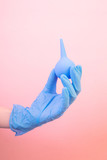 Hand in a blue medical glove with blue enema (clyster) on a pink background. The concept of medicine, vaccination, health. Minimalism, place for text.