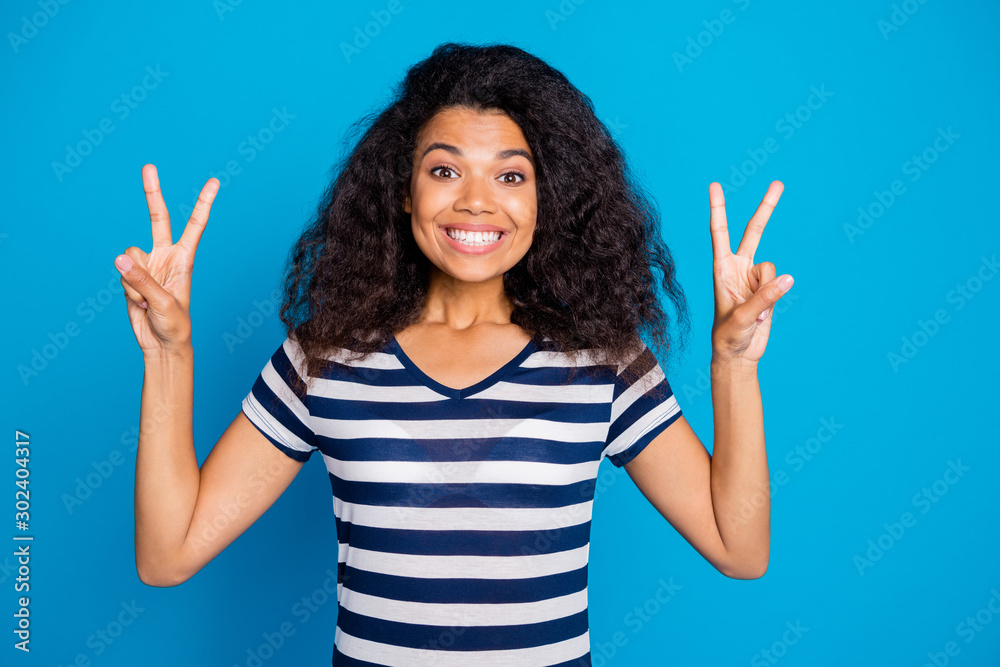 Photo of cheerful positive nice pretty cute charming girlfriend showing you double v-sign showing her white teeth in striped t-shirt isolated vivid color blue background Photo of cheerful positive nice pretty cute charming girlfriend showing you double v-sign showing her white teeth in striped t-shirt isolated vivid color blue background