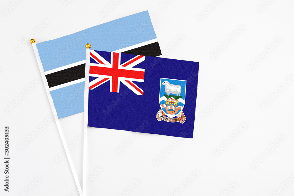 Fototapeta premium Falkland Islands and Botswana stick flags on white background. High quality fabric, miniature national flag. Peaceful global concept.White floor for copy space.