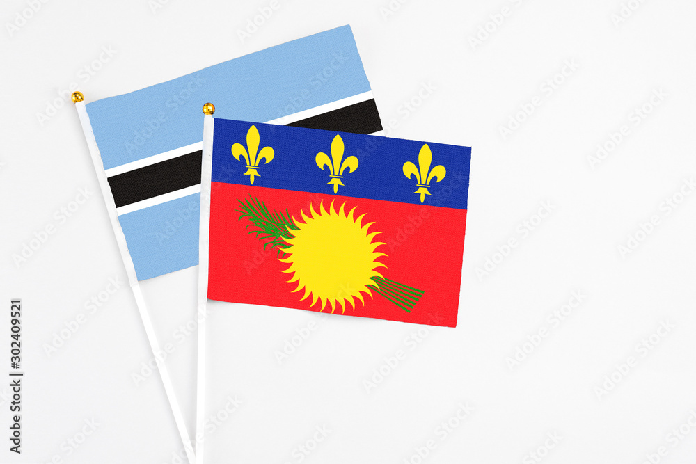 Naklejka premium Guadeloupe and Botswana stick flags on white background. High quality fabric, miniature national flag. Peaceful global concept.White floor for copy space.