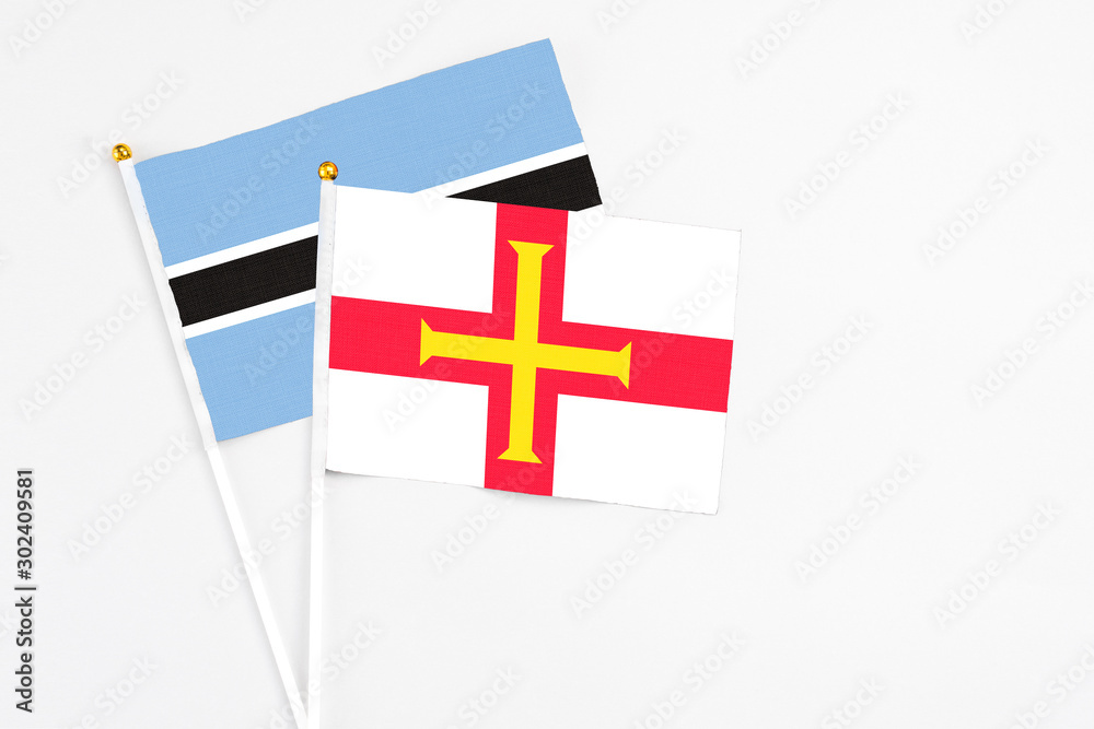 Guernsey and Botswana stick flags on white background. High quality fabric, miniature national flag. Peaceful global concept.White floor for copy space.