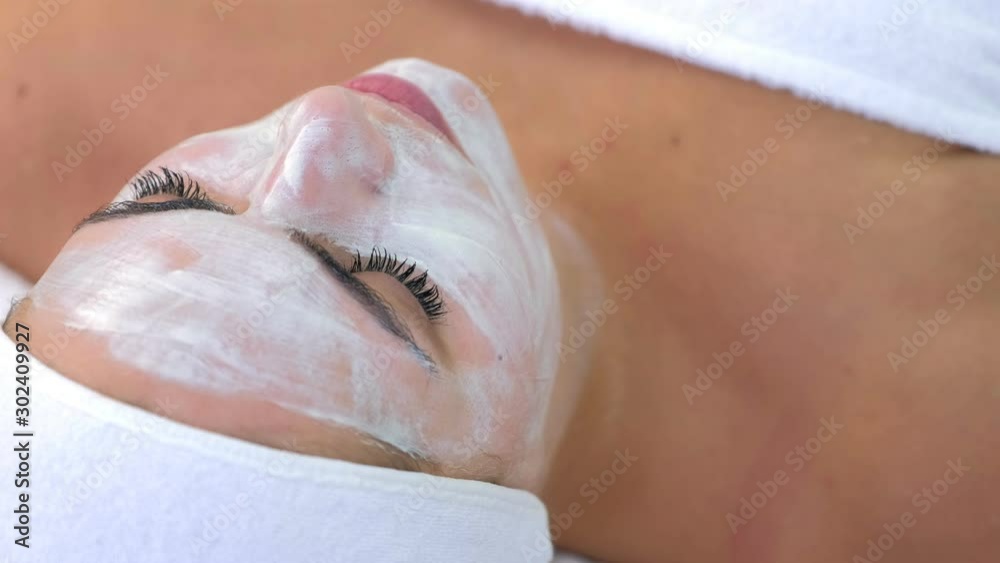 Portrait of woman laying in spa cosmetology salon with white mask on face. Beauty facial skincare procedure to patient in cosmetology clinic, face closeup. Beauty industry concept. Portrait of woman laying in spa cosmetology salon with white mask on face. Beauty facial skincare procedure to patient in cosmetology clinic, face closeup. Beauty industry concept.