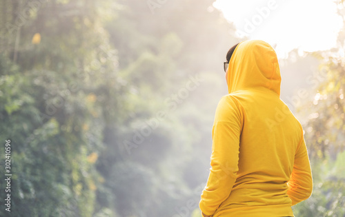 Woman traveler in yellow sweater with hood is standing and looking to nature.