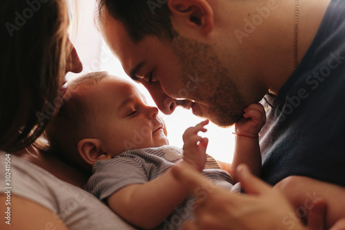 Baby with his parents playing on the bed. Happy family at home. Lifestyle cozy photos. Little boy 4 months old