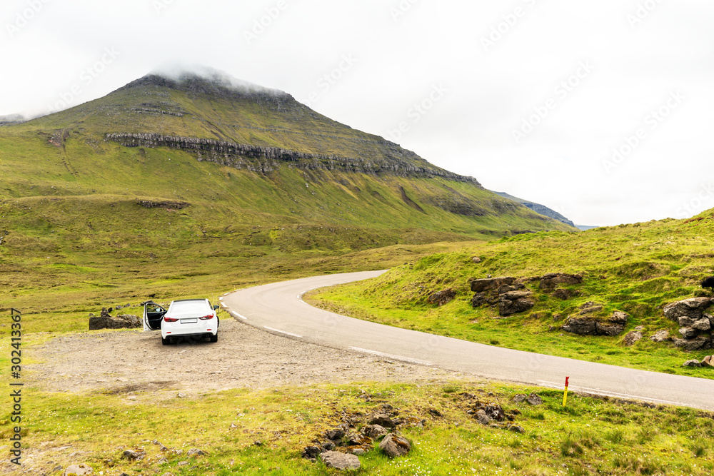 Road trip adventure on Faroe Islands. Car  on roadside, green mountains covered with clouds.