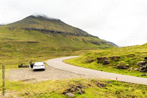 Road trip adventure on Faroe Islands. Car on roadside, green mountains covered with clouds.