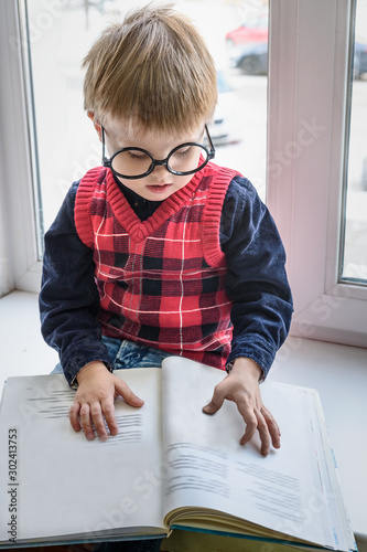 Obraz na płótnie Little boy in glasses with book in library on window w salonie