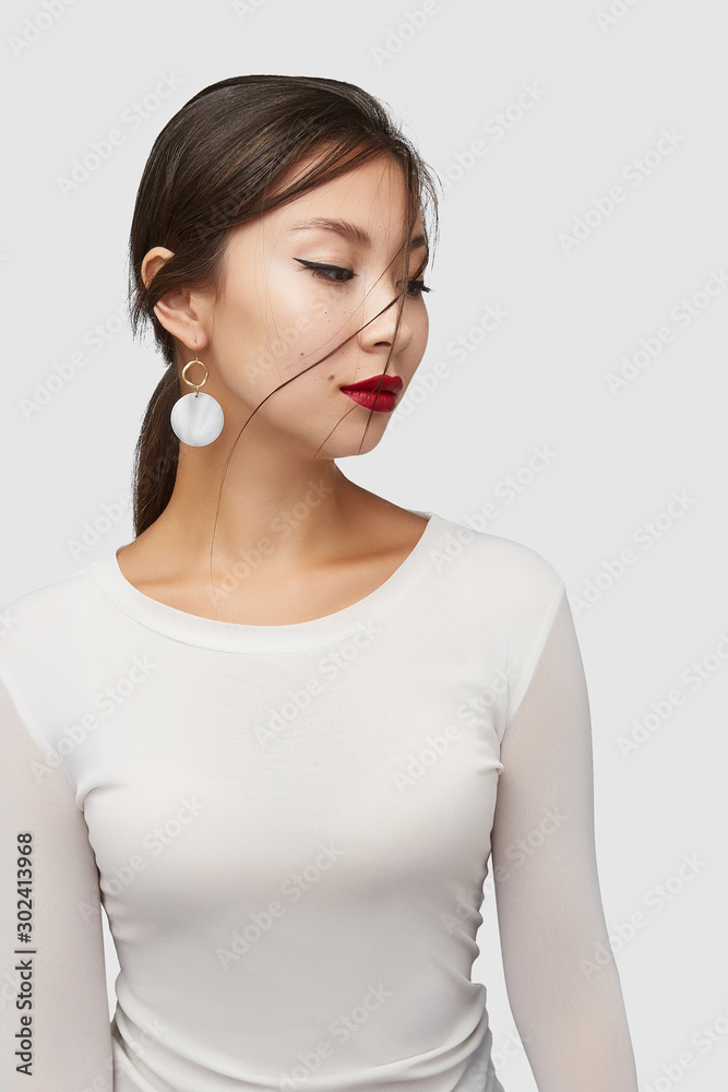 Medium shot of a young Asian woman in an ivory white blouse and with a hook earring with a golden wavy ring and a round nacre disc. Medium shot of a young Asian woman in an ivory white blouse and with a hook earring with a golden wavy ring and a round nacre disc.