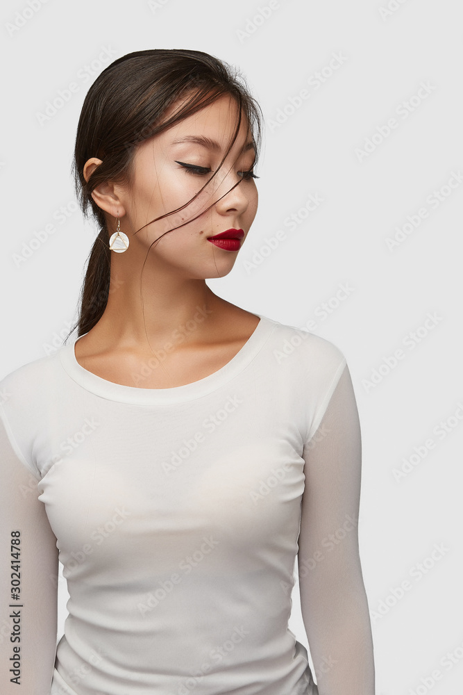 Medium shot of a young Asian woman in an ivory white blouse and with a golden hook earring with a nacre disc and a golden triangle frame. Medium shot of a young Asian woman in an ivory white blouse and with a golden hook earring with a nacre disc and a golden triangle frame.