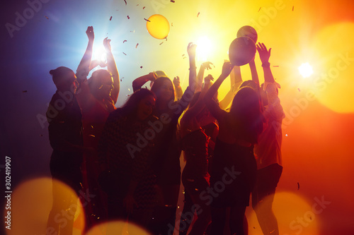 Memories. A crowd of people in silhouette raises their hands on dancefloor on neon light background. Night life, club, music, dance, motion, youth. Yellow-blue colors and moving girls and boys.