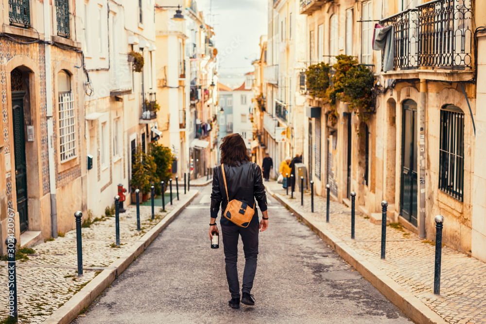 Long haired portuguese man walking through the narrow street of Lisbon carrying portuguese wine