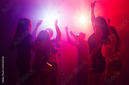 Shadows. A crowd of people in silhouette raises their hands on dancefloor on neon light background. Night life, club, music, dance, motion, youth. Purple-pink colors and moving girls and boys.