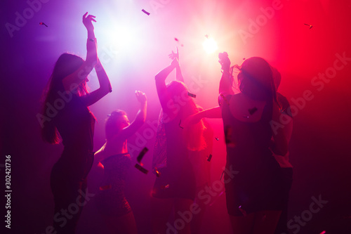 Celebrating. A crowd of people in silhouette raises their hands on dancefloor on neon light background. Night life, club, music, dance, motion, youth. Purple-pink colors and moving girls and boys.
