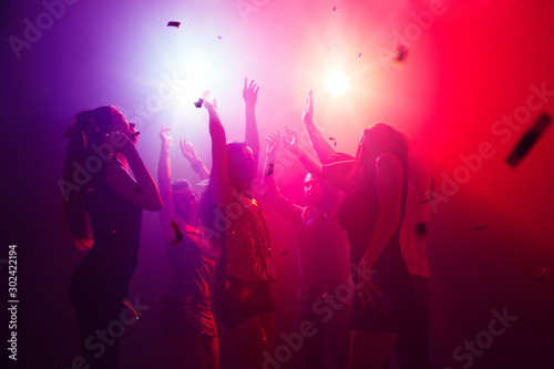 Bass. A crowd of people in silhouette raises their hands on dancefloor on neon light background. Night life, club, music, dance, motion, youth. Purple-pink colors and moving girls and boys. photo
