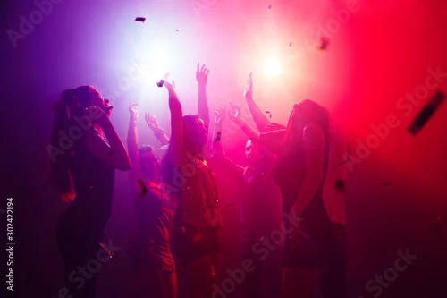 Obraz Bass. A crowd of people in silhouette raises their hands on dancefloor on neon light background. Night life, club, music, dance, motion, youth. Purple-pink colors and moving girls and boys.