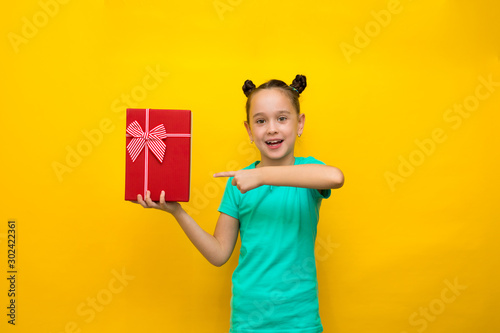happy little girl standing isolated over yellow background holding red gift box. Looking camera, smiling broadly