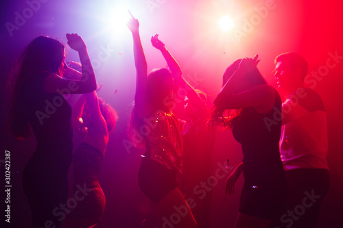 No troubles. A crowd of people in silhouette raises their hands on dancefloor on neon light background. Night life, club, music, dance, motion, youth. Purple-pink colors and moving girls and boys.