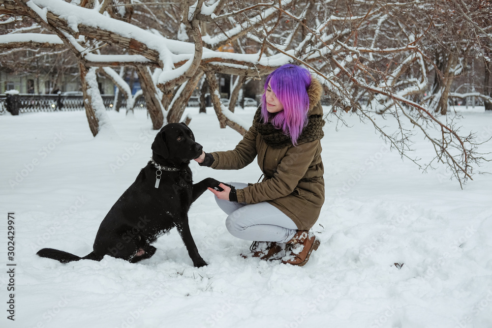 A young woman plays with her pet black Labrador outside in winter.