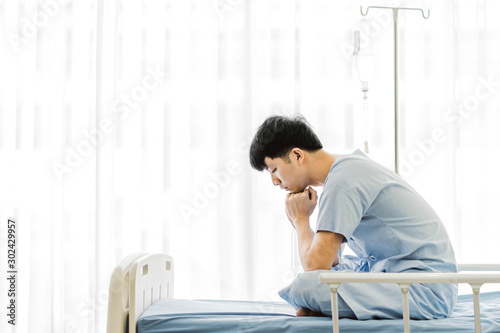 Patient asian man 25 year old Wear a sick suit feeling unwell and worry, sit in a bed at hospital. Asian patient young male 25s is a flu feel not good sit on a bed in the room. white background photo