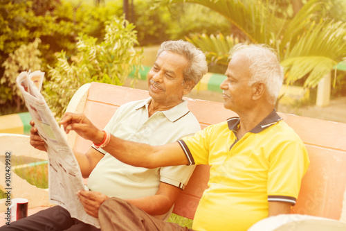 Two happy senior men reading newspaper at park outdoor - elderly friends enjoying moring news - Concept of happy older men lifestyle.