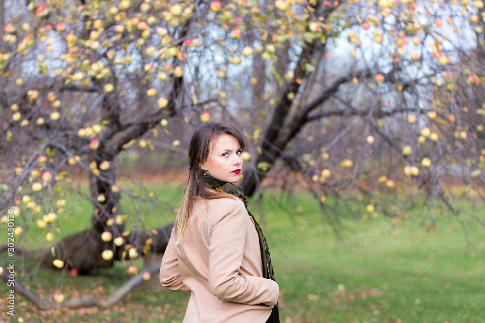 Medium horizontal photo of pretty young woman with long straight hair wearing beige coat staring over her shoulder with serious expression in front of late fall landscape Medium horizontal photo of pretty young woman with long straight hair wearing beige coat staring over her shoulder with serious expression in front of late fall landscape