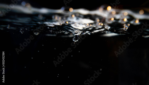Closeup water drop and air bubbles in water in black background.