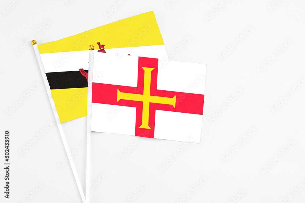 Guernsey and Brunei stick flags on white background. High quality fabric, miniature national flag. Peaceful global concept.White floor for copy space.