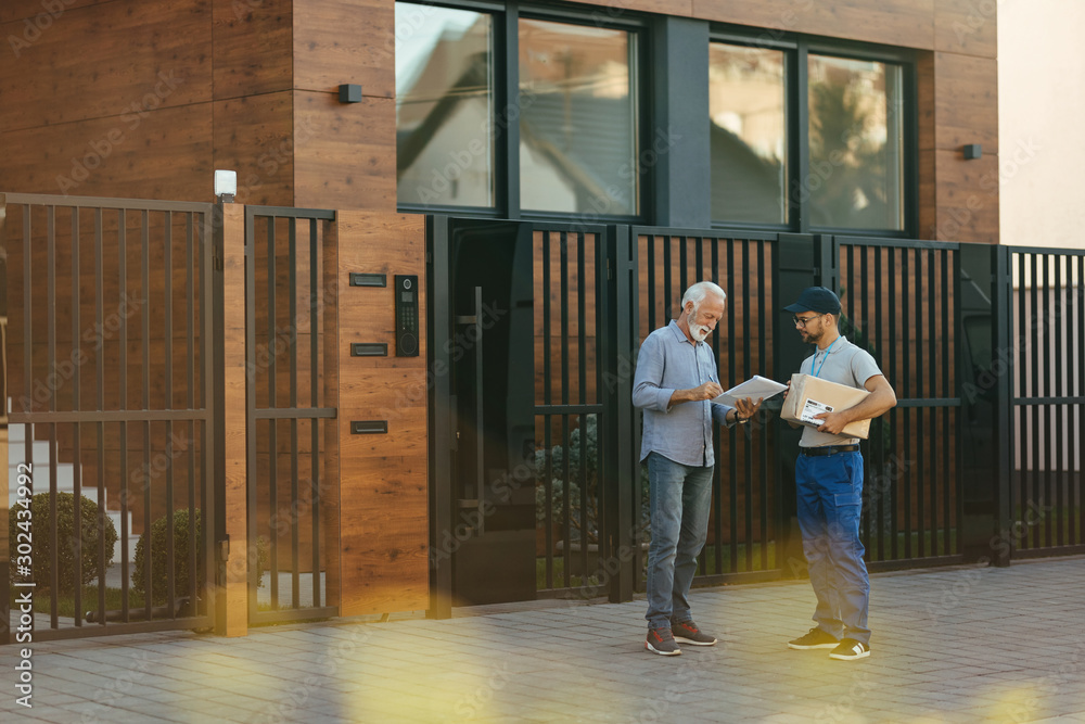 Mature man signing paperwork while getting package delivered at his home.