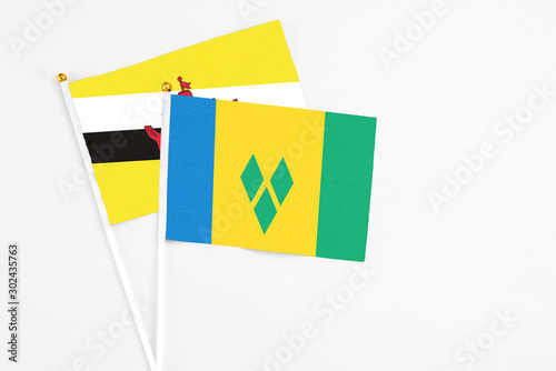 Saint Vincent And The Grenadines and Brunei stick flags on white background. High quality fabric, miniature national flag. Peaceful global concept.White floor for copy space.