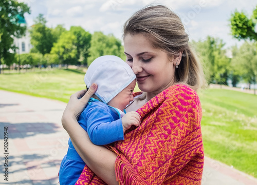 A young girl is holding a baby in her arms.  Mom and son are walking in the park.