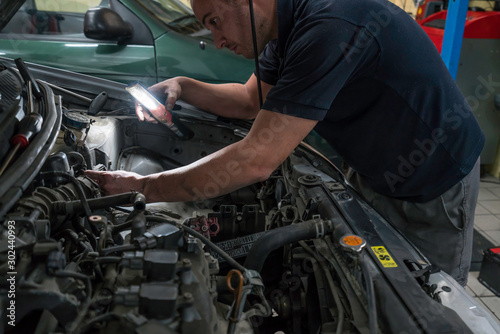 Auto mechanic working on car engine in mechanics garage. Car repair service.
